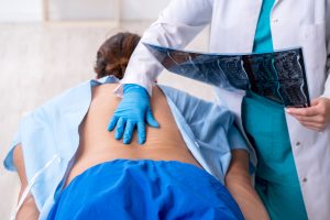 Doctor examining patient's back, holding X-ray.