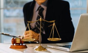 A surgery negligence lawyer researching a claim at a table with scales, gavel and open laptop. 