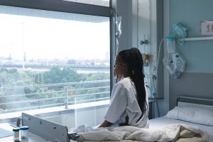 A woman sits on a bed and looks out of a hospital room window