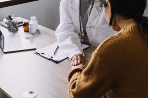 A doctor seated at a table comforts a patient during a consultation
