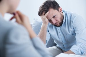 A man in a light blue shirt puts his head in his hand during a therapy session